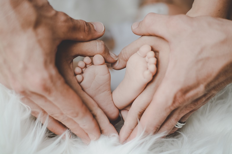 Zwei Hände von Eltern, die die Babyfüße ihres Kindes als Herzform halten